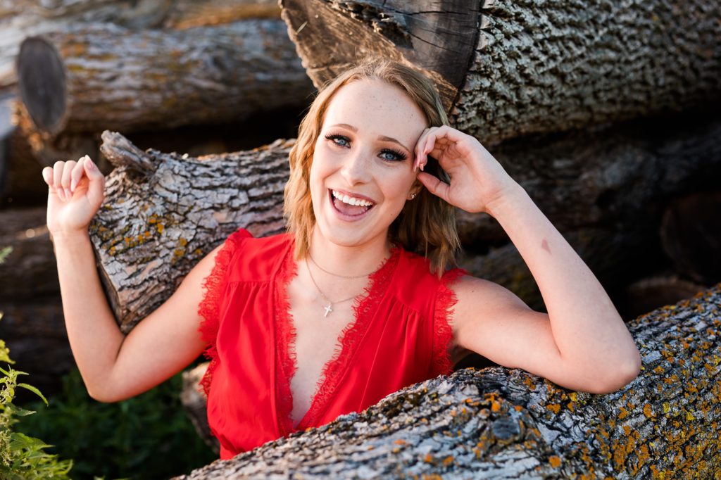 High School Senior Portrait Wearing a Red Dress next to Logs | Amber Langerud Photography