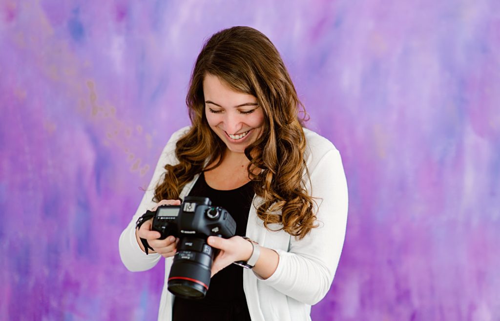 Wedding Photographer Holding Camera in Front of Purple Background | Amber Langerud Photography