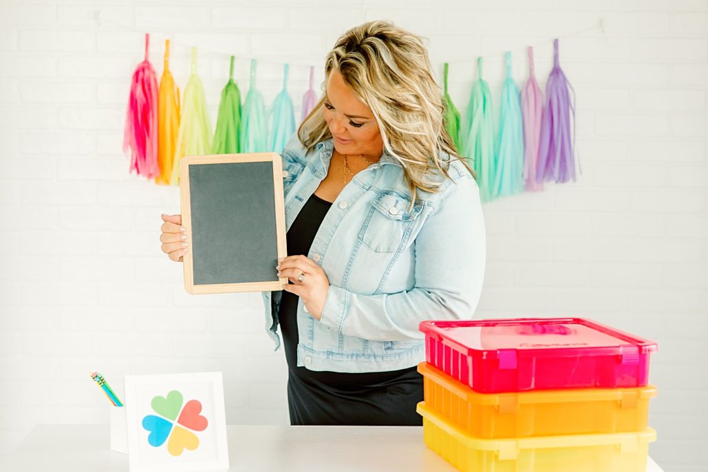 teacher influencer holding chalk board with colored organizer bins on desk