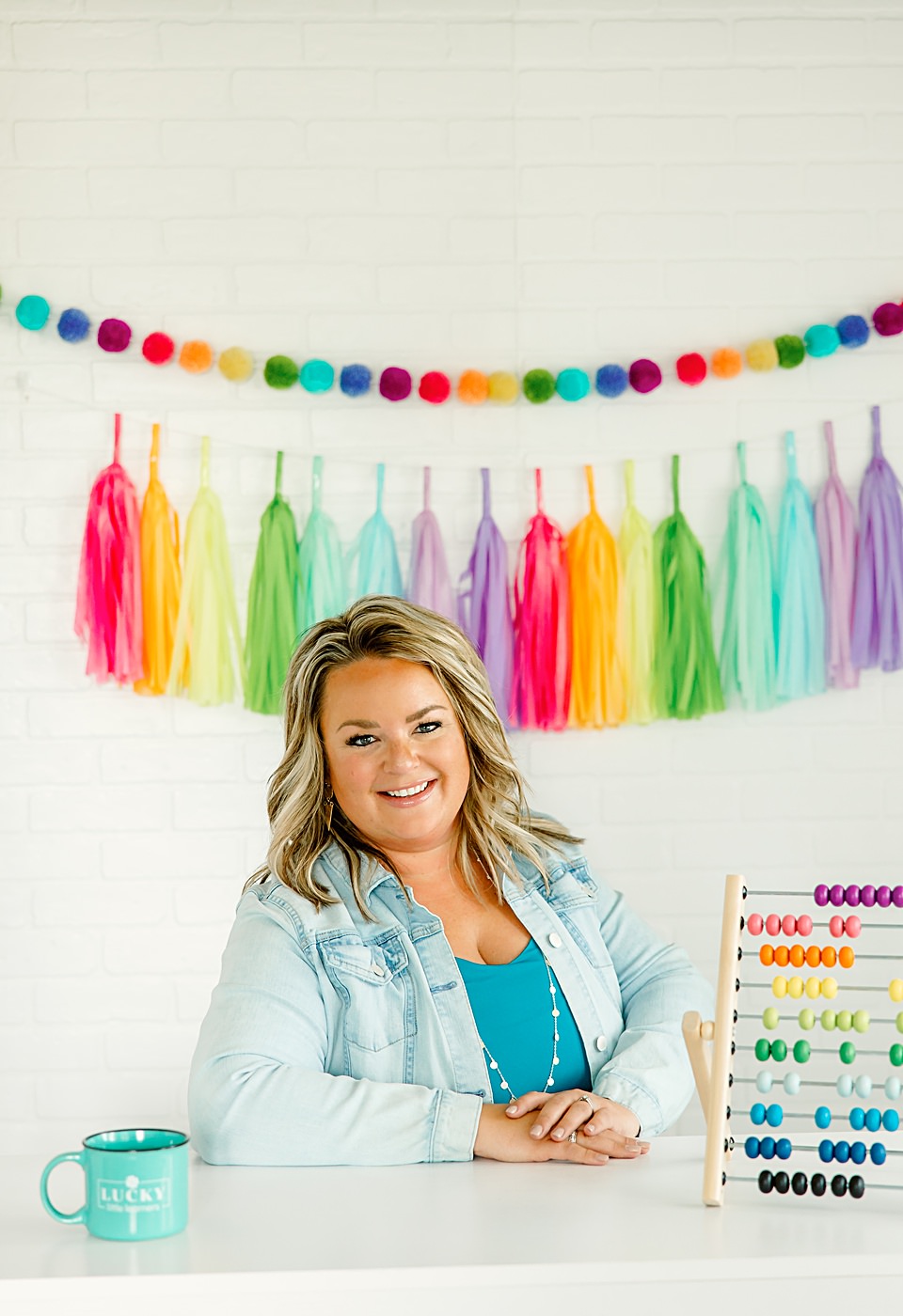 Curriculum Designer Brand Photography Session, headshot standing at white desk in front of a rainbow colored background