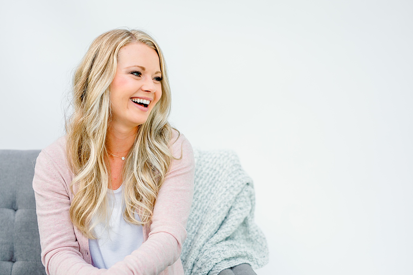 podcaster wearing pink cardigan sitting on a grey couch during brand photography session