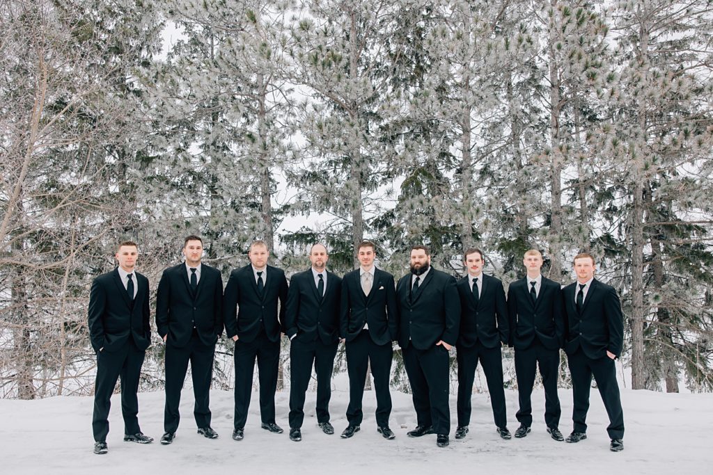 Groomsmen posed in the snow in front of pine trees at the Timbers Event Center in Staples, MN