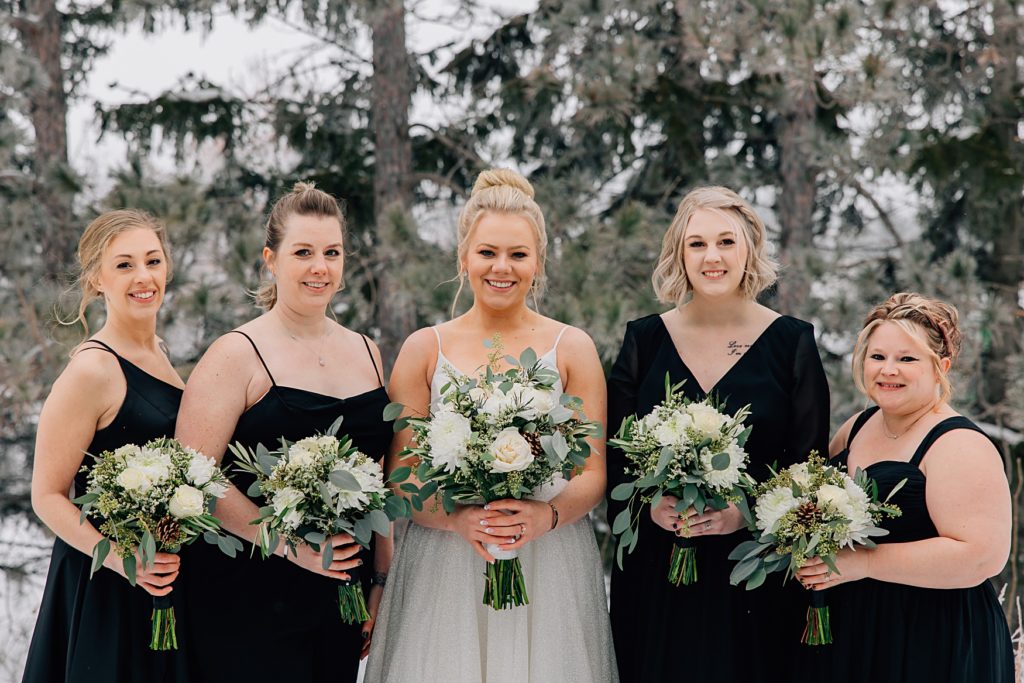 bridesmaids posed in the snow in front of pine trees at the Timbers Event Center in Staples, MN