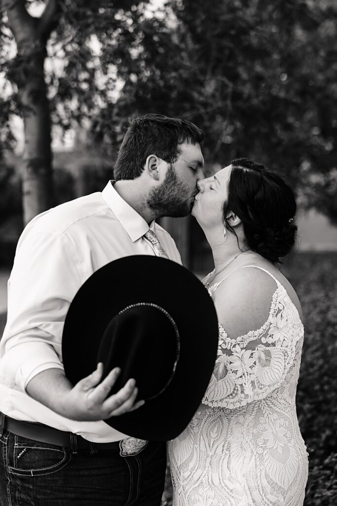 bride and groom kissing behind cowboy hat