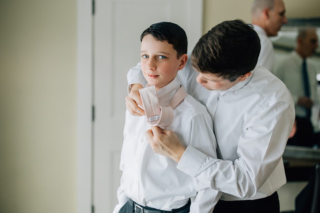 Groom helping his brother in law tie his tie at the Lafayette Club in Minnetonka Beach, MN