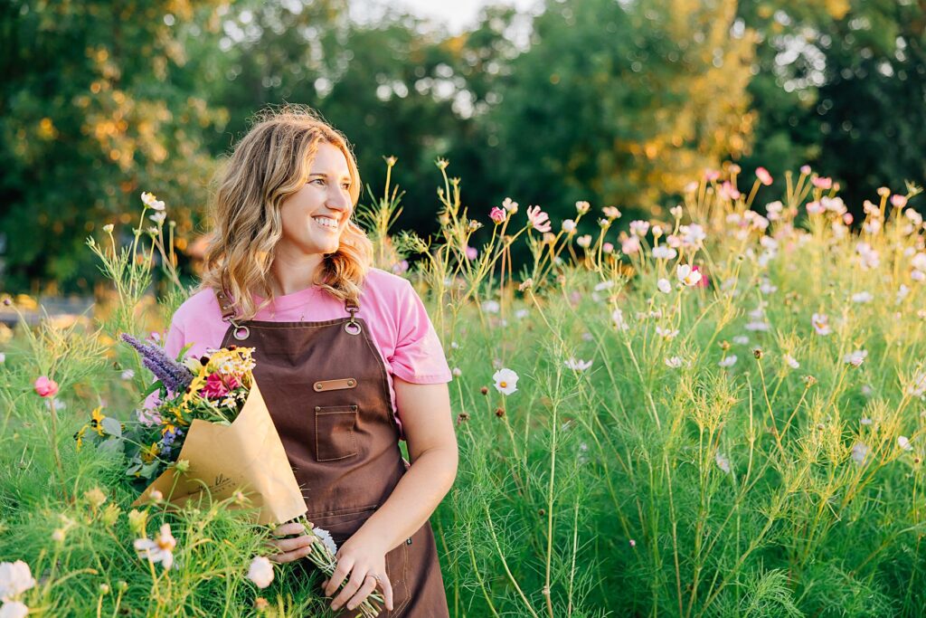 flower farmer standing in a field of flowers holding a bouquet wearing her uniform brand photography outfit
