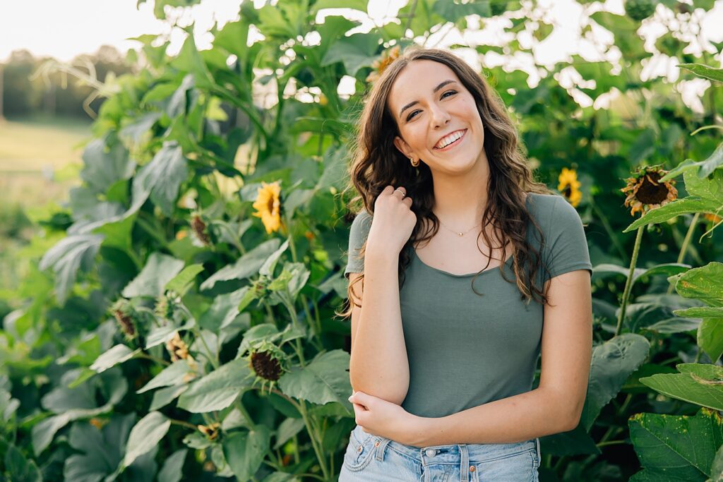 photo of a senior girl standing in front of a gourd arch and sunflowers